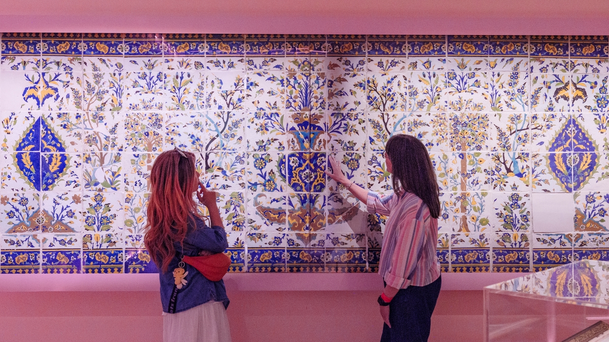 Two people standing next to a large tile panel.