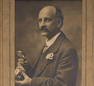 Sepia photograph of a man in a suit holding a magnifying glass